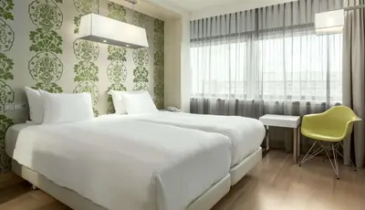 a bedroom with a large white bed and a yellow chair at NH Amsterdam Zuid in Amsterdam