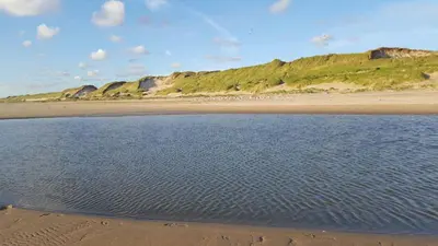 a view of a beach with rocks in the background at Zomerhuis Duinzicht in Egmond aan den Hoef