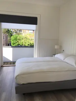 a white bedroom with a large bed and a window at Studio De Laan in Zandvoort