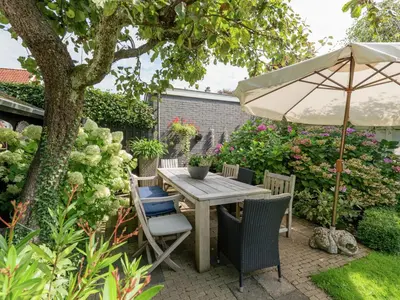 a table and chairs with an umbrella in a garden at Apartment in Bergen near Schoorl Dunes in Bergen