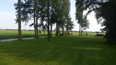 a grassy field with trees and a river at Appartement De Molshoop II in Landsmeer