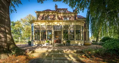 an old house with large windows and a tree at Logement aan de Vecht in Breukelen