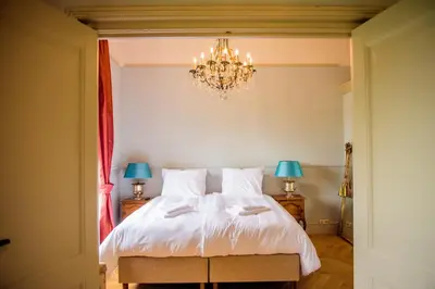 a bedroom with a white bed with a chandelier at Logement aan de Vecht in Breukelen