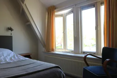 a bedroom with two windows and a bed and a chair at B&B - Pension Het Oude Dorp in Katwijk