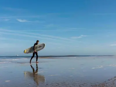 a man walking on the beach with a surfboard at Holiday Home in Noordwijk near Beach in Noordwijk