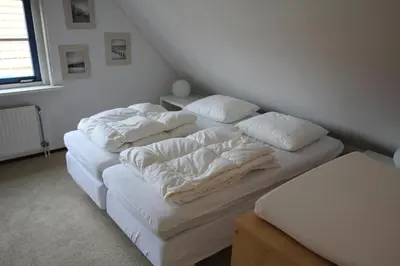 two beds in a room with white sheets and pillows at Vakantiehuis Zeeduinenbos in Schoorl