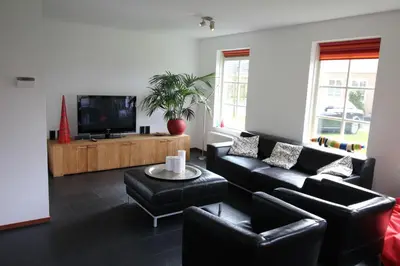 a living room with black leather furniture and a flat screen tv at Vakantiehuis Zeeduinenbos in Schoorl