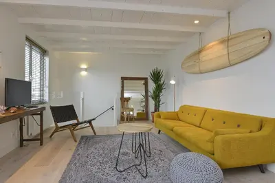 a living room with a yellow couch and a surfboard on the wall at Endless Summer Beach Apartments in Zandvoort