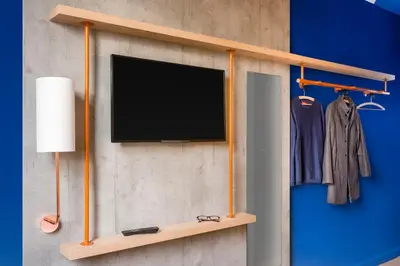 a tv hanging on a wall with a wooden shelf at ibis budget Amsterdam City South in Amstelveen