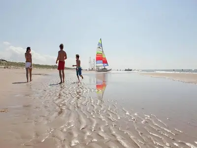 a group of people standing on a beach with a sailboat at Holiday Home Egmond near Beach in Egmond aan Zee