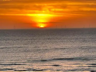 a sunset over the ocean with wind turbines in the distance at Holiday Home Egmond near Beach in Egmond aan Zee