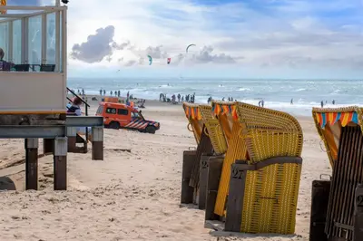 a beach with yellow chairs and people in the ocean at Carpe Diem Egmond aan Zee by Urban Home Stay in Egmond aan Zee