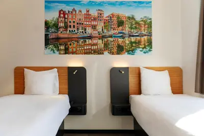 two beds in a room with paintings on the wall at easyHotel Amsterdam Arena Boulevard in Amsterdam