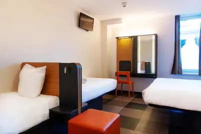 a room with two beds and a chair and a mirror at easyHotel Amsterdam Arena Boulevard in Amsterdam