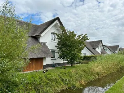 a house with a thatched roof next to a river at Holiday Home Alk 8-1 by Interhome in Noordwijkerhout