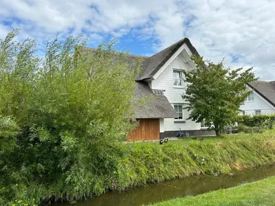 a house with a thatched roof next to a river at Holiday Home Tapuit 8-1 by Interhome in Noordwijk