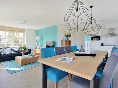 a dining room and living room with a table and blue chairs at Holiday Home Tapuit 8-2 by Interhome in Noordwijk