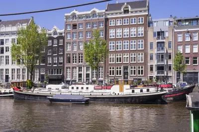 two boats are docked in the water near buildings at Luxurious 110m² 3br Houseboat in Amsterdam Centre! in Amsterdam