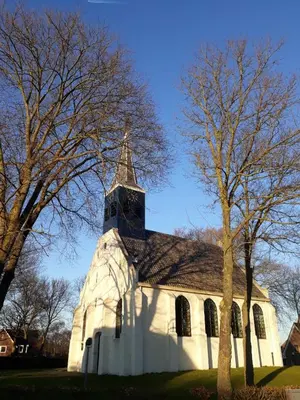 a white church with a steeple and a tree at Duinkant in Groet