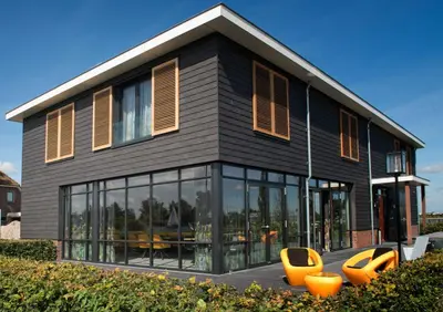 a black house with orange chairs in front of it at als het golft in Roelofarendsveen
