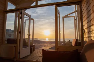 an open door to the beach at sunset at Surf en beach strandhuisjes in Katwijk