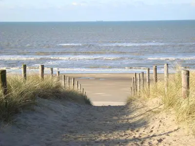 a sandy beach next to the ocean with a fence at B&B Mol in Katwijk aan Zee