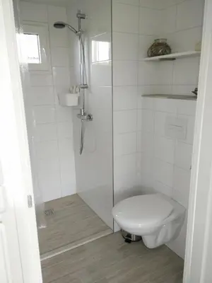 a white bathroom with a toilet and a shower at Coast Holiday Appartements in Dirkshorn