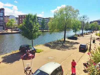 a woman standing on a sidewalk next to a river at Jordaan View in Amsterdam