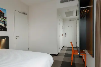 a bedroom with a white bed and a orange chair at easyHotel Amsterdam Zaandam in Zaandam
