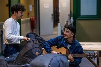 a man playing a guitar while another man looks at him at Shelter City Christian Hostel in Amsterdam