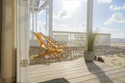 a porch with two chairs and a plant on the beach at Kusthuisjes in Katwijk