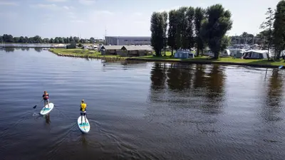 two people are on paddle boards in the water at Jachthaven Nieuwboer in Bunschoten