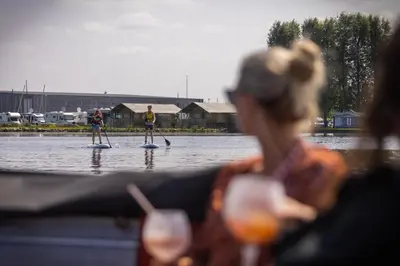a woman sitting on a boat watching two people on paddle boards in the water at Jachthaven Nieuwboer in Bunschoten