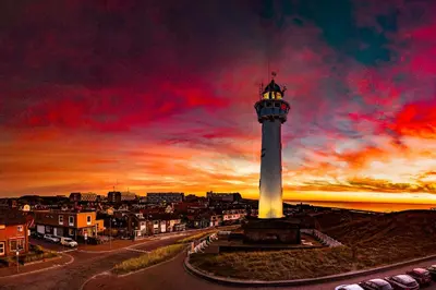 a lighthouse on a hill with a sunset in the background at Aan Zee en Duin in Egmond aan Zee