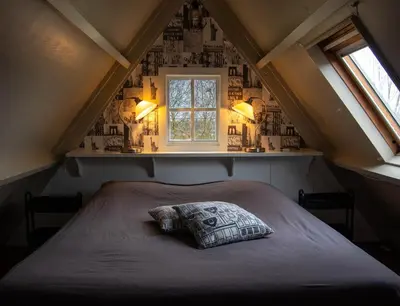 a bed with a pillow in a room with a window at B&B Saense huisje in Assendelft