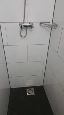 a white tiled bathroom with a shower with a drain at Hotel Schroder in Amsterdam