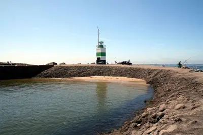 a lighthouse on a beach with a body of water at Hotel Velsen in IJmuiden