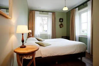 a bedroom with a bed with a table and two windows at De Sfeerstal in Nieuwveen