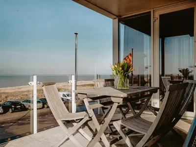 a wooden table and chairs on a deck with the beach at Apartment by the Beach with Sea Views in Egmond aan Zee