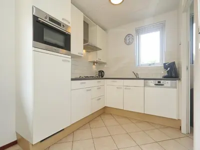 a white kitchen with white cabinets and a window at Holiday Home in Noordwijk with Sunny Garden in Noordwijk aan Zee