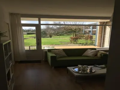 a living room with a green couch and a large window at Modern Apartment in Noordwijk near the Sea in Noordwijk