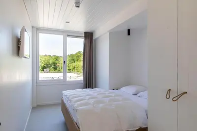 a white bedroom with a bed and a window at Duinappartementen Schoorl in Schoorl