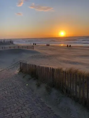 a sunset on a beach with the ocean and a fence at Benny's Beach House 1 in Zandvoort