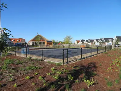 a fence around a tennis court with houses in the background at Luxurious Water Villa in Uitdam