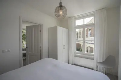 a white bedroom with a bed and a window at Luxury Upstairs & Downstairs Apartments in Zandvoort