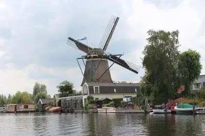 a windmill on the water next to a house at Bed & Breakfast Kortenhoefsedijk in Kortenhoef