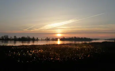 a sunset over a field with the sun in the sky at De Vooroever in Wervershoof