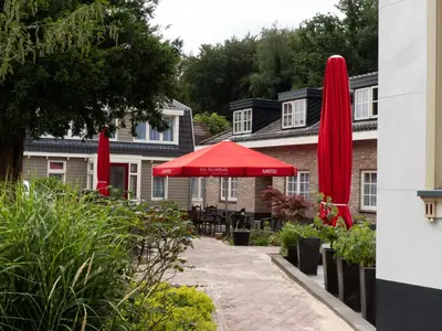 a patio with red umbrellas and tables in front of a building at Hotel-Restaurant Het Rechthuis in Muiderberg