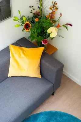 a gray couch with a yellow pillow and a vase of flowers at i hotel in Amsterdam
