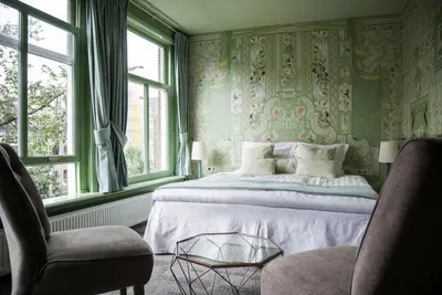 a bedroom with a bed and a chair and windows at 't Hotel in Amsterdam